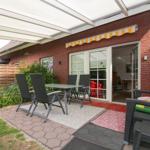 Terrasse mit Tisch, Stühlen und Pavillon. Durchgang in Wohnbereich. Garten mit Pflanzen und Zaun.