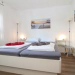 Schlafzimmer mit Doppelbett, zwei Stehlampen und Wandbild.
