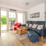 Wohnzimmer mit blauem Sofa, rotem Sessel und Holztisch. Durchgang zur Terrasse.