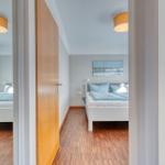 Schlafzimmer mit Bett, Wandbild und Holzboden. Zwei Deckenleuchten sichtbar.