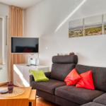 Wohnzimmer mit Sofa, Fernseher und Fenster zum Balkon.