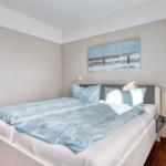 Schlafzimmer mit Bett, Wandbild und Stehlampe.