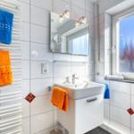 Badezimmer mit Waschbecken, Spiegel und Heizkörper mit Handtüchern.