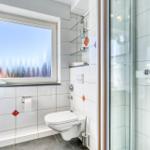 Badezimmer mit Dusche, Toilette und Waschbecken. Fenster mit Blick auf Wald.