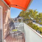 Terrasse mit Liegestuhl und orangefarbenem Markisenüberdachung. Blick auf Straße und Bäume.