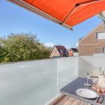 Terrasse mit orangefarbenem Markisenüberdachung und Glastrennwand. Tisch mit Geschirr und Gläsern.