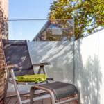 Terrasse mit Liegestuhl und Fußstütze, grüner Decke, Backsteinwand und Glasgeländer.