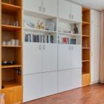 Große weiße und holzfarbene Schränke mit Büchern und Dekorationsgegenständen. Holzfußboden und Vorhang.