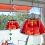 Hängende rote Glaslampen über einem Tisch mit Blick auf Balkon und Grün.