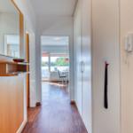 Flur mit Schrank, Spiegel und Blick in Wohnbereich mit Fenster.