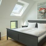 Schlafzimmer mit Dachschrägen, Dachfenstern und Bett mit weißen Kissen.