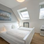 Schlafzimmer mit Dachschrägen, Bett, Fenster und Wandbild.