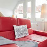 Rotes Sofa mit Kissen und Decke vor Fenster