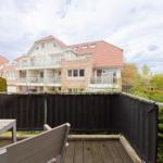 Terrasse mit Tisch und Stühlen, Blick auf Wohnhaus mit Balkon und Garten.