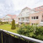 Blick auf Wohnhaus mit Balkon, Garten und Bäumen unter bewölktem Himmel.