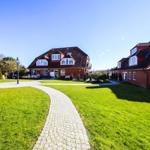 Zwei rote Häuser mit Dachgauben stehen im Garten mit Kiesweg.