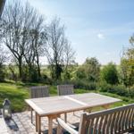 Terrace with table and chairs, view of green meadows and trees.