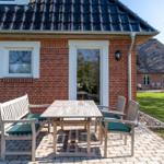 Red brick house with terrace and garden furniture. Courtyard with thatched roof house.