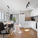 Kitchen and dining area with white built-in kitchen, wooden floor, and large dining table.