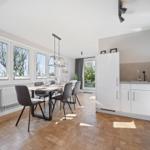 Dining room with table, chairs, and windows. Kitchen with worktop and cabinets.