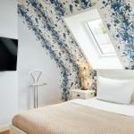 Schlafzimmer mit Dachfenster, blauem Tapetenmuster und Fernseher an der Wand.