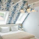 Schlafzimmer mit blauem Muster, Dachfenstern und Bett mit weißen Kissen.