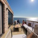 Terrasse mit Sitzgelegenheiten und Meerblick. Holztisch und Sofa mit Kissen.