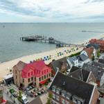 Haus mit rotem Dach an Strand, Blick auf Pier und See.