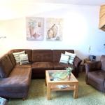 Ein Wohnzimmer mit braunem Sofa, Holz-Tisch und Wandbildern.