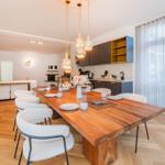 Essbereich mit Holztisch, weißen Stühlen und moderner Küche im Hintergrund.