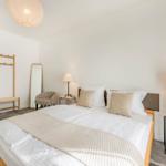 Schlafzimmer mit Bett, Nachttisch, Kleiderständer und Spiegel.