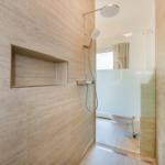 Dusche mit Duschbrause, eingelassene Ablage und Toilette hinter Glaswand.