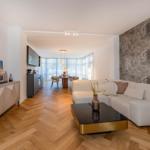 Wohnzimmer mit Sofa, Couchtisch und TV. Küche und Essbereich im Hintergrund.