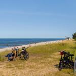 Zwei Personen sitzen auf einer Bank am Strand. Fahrräder stehen daneben.