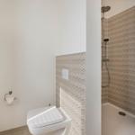 Badezimmer mit Dusche und WC. Duschwand mit Muster. Beige Vorhang.