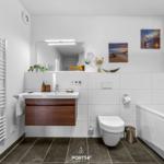 Badezimmer mit Badewanne, Waschbecken und Toilette. Weiße Fliesen und Holzfront.