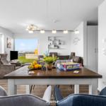 Esszimmer mit Tisch, Stühlen und Blick auf Garten. Große Uhr an der Wand.