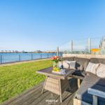 Terrasse mit Sofa, Tisch und Meerblick. Grünfläche und Wasser im Hintergrund.