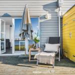 Terrasse mit Liegestuhl, Grill und geschlossenem Sonnenschirm neben gelbem Schuppen.