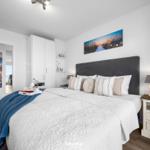 Schlafzimmer mit Bett, Nachttisch und Kleiderschrank. Wandbilder zeigen Strandmotiv.