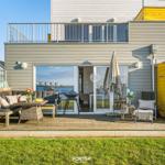 Terrasse mit Sitzgruppe, Grill und Blick aufs Wasser.
