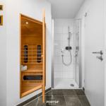 Sauna und Dusche in einem Raum mit Holz und weißen Wänden.