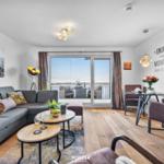 Wohnbereich mit Sofa, Esstisch und Balkonblick auf Wasser.