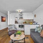 Wohnung mit Küche, Sofa und Fernseher. Holzboden und weiße Wände.