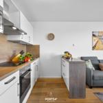 Küche mit Arbeitsfläche, Herd und Mikrowelle. Wohnbereich mit Sofa und Wandbild.