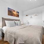 Schlafzimmer mit Bett, Nachttisch und Wandbild. Holzboden und weiße Wände.