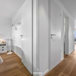 Schlafzimmer mit Bett, Nachttisch und Wandbild. Flur führt zum Wohnbereich mit Balkon.