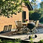 Terrasse mit Tisch, Stühlen und Grill neben Backsteinhaus.