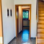 Flur mit Holztreppe, Bildern an der Wand und Blick in die Küche.