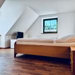 Schlafzimmer mit Dachschrägen, Holzboden und zwei Fenstern mit grünen Rahmen.